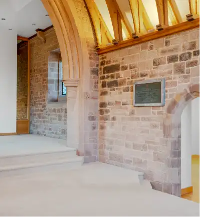 Living pace of chapel with exposed stone wall and beams with cream carpet